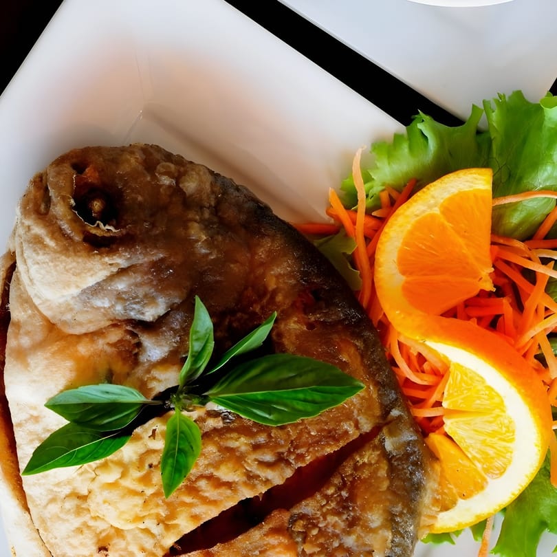 Crispy fried whole fish garnished with fresh basil, orange slices, shredded carrots, and lettuce.