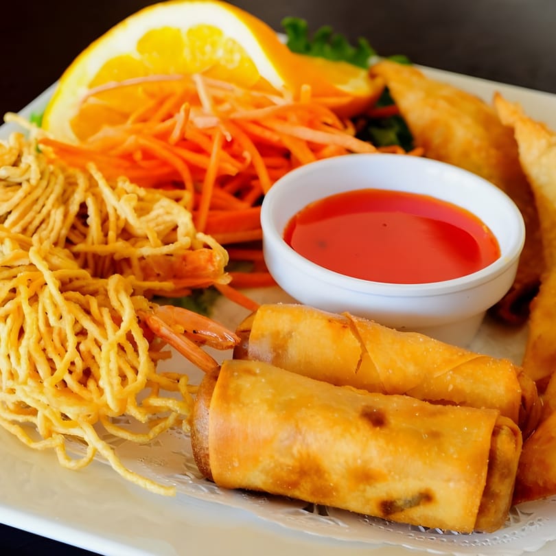 Thai appetizer platter with fried spring rolls, crispy noodles, shrimp, shredded carrots, and dipping sauce.