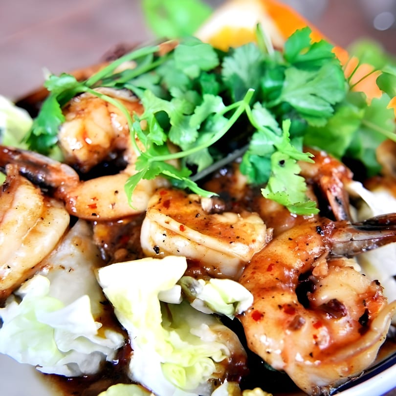 Close-up of Thai garlic shrimp with fresh cilantro and cabbage, garnished with an orange slice.